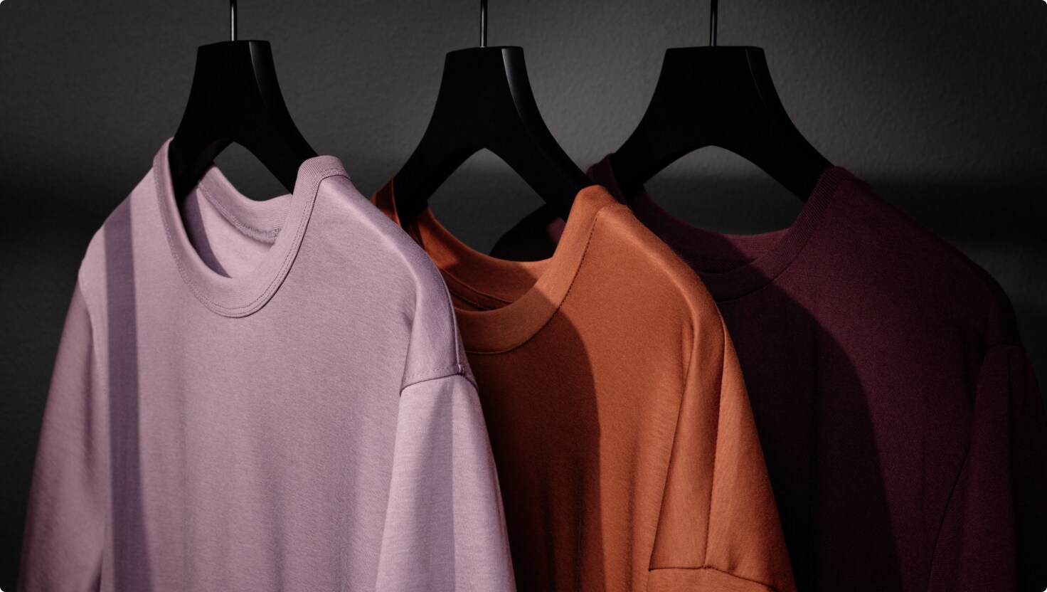 Colorful sweaters hanging in a row on hangers.